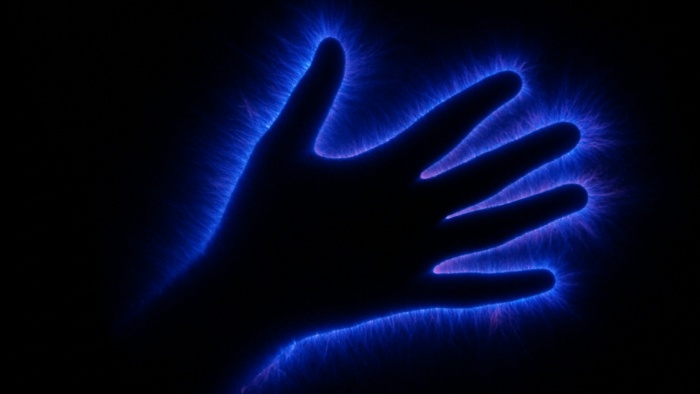Fotografia de uma mão com efeito de descarga elétrica azul ao redor, capturada pela técnica de fotografia Kirlian.